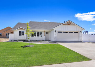 A simple white house with a gray roof and wood accents set against a green lawn and a bright blue sky