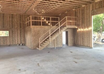 An unfinished framed interior of a shop with stairs leading up.