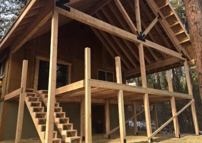 An unfinished framed building set against a pine forest and a blue sky