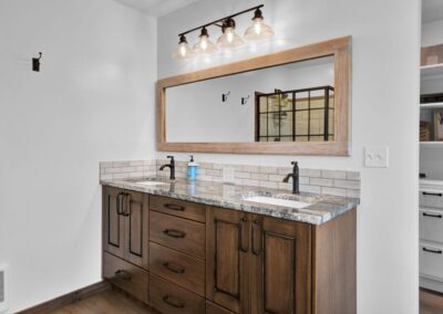 A simple double sink with wood cabinets and a big mirror behind