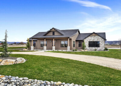 A brown house with a black roof and brick accents with a circle driveway set against a blue sky